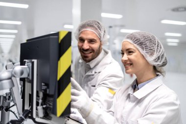 Fabrikada birlikte çalışan çalışanlar bilgisayar ekranında üretim makinesini kontrol ediyorlar..