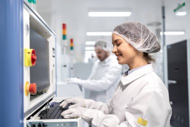 Üretim hattı ve endüstriyel makine üzerinde çalışan kadın fabrika çalışanı.