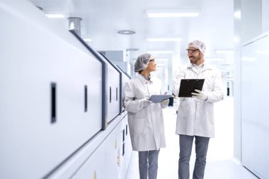 Deneyimli yöneticiler modern üretim fabrikasında yürüyor ve kalite kontrolü yapıyorlar..