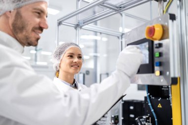 Fabrikada otomatikleştirilmiş üretim makinesini çalıştıran çalışkan çalışanlar.