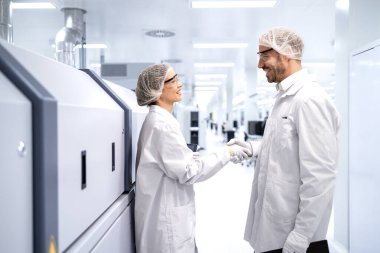 Üretim hattı işçileri fabrikada el sıkışıyor. Çalışanlar arasında iyi bir işbirliği.