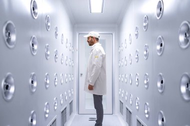 Fabrika işçisi endüstriyel hava üfleme tünelinde duruyor. Üretim hattına girmeden önce toz ve parçacıkları temizliyor..