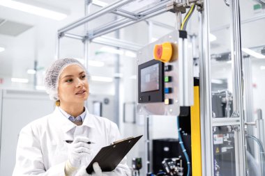 Modern endüstriyel makinenin üretim sürecini kontrol eden ve izleyen kadın fabrika işçisi.