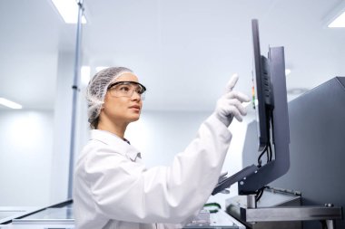 Kadın fabrika işçisi gelişmiş endüstriyel makinede üretim sürecini izliyor..