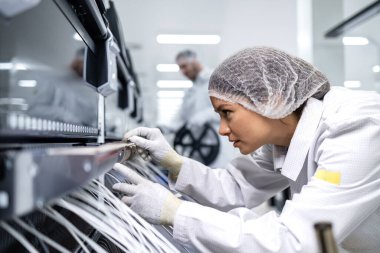 Deneyimli fabrika işçisi üretim makinesi üzerinde çalışıyor ve elektronik endüstrisindeki kabloları birbirine bağlıyor..