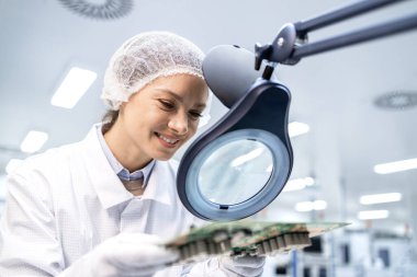 Elektronik çip endüstrisinde çalışıyor. Kalite kontrol çalışanı basılı devre kartlarını otomotiv endüstrisi için kontrol ediyor.