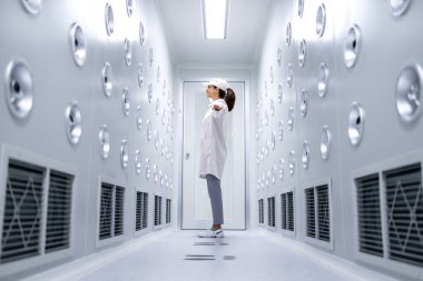 Fabrika işçisi endüstriyel hava üfleme tünelinde duruyor. Üretim hattına girmeden önce toz ve parçacıkları temizliyor..