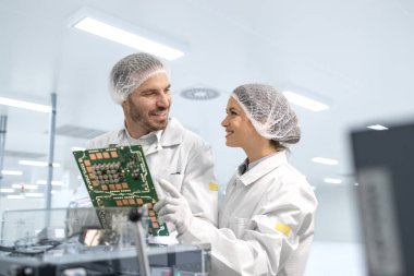 Deneyimli işçiler elektronik imalat fabrikasında mikroçiplerin kalitesini ve basılı devre kartlarını kontrol ediyorlar..