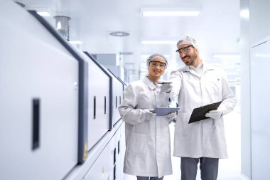 Deneyimli fabrika teknisyenleri üretim salonunda yürüyor ve otomatik makineleri kontrol ediyorlar..