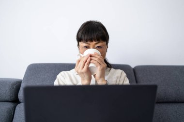 Güzel Asyalı kadın çay içiyor ve dizüstü bilgisayara bakıyor..