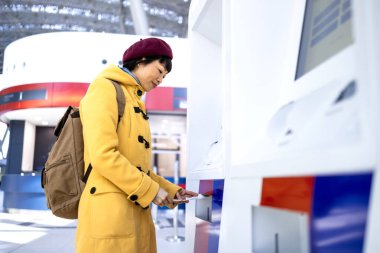 Sırt çantalı bir bayan yolcu havaalanındaki self servis gişesinde bilet alıyor..