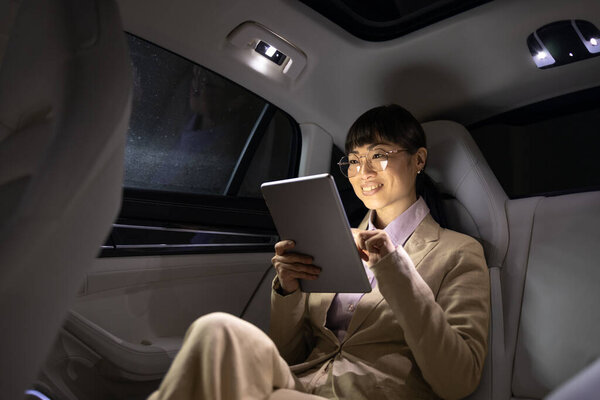 Female Asian business person traveling in luxurious limousine and having important video call.