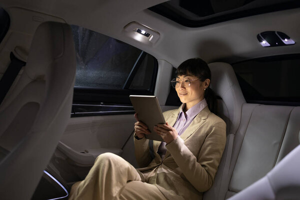 Wealthy Asian businesswoman going on business trip in luxury automobile while having conference call.