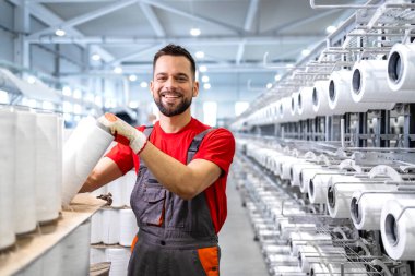 Tekstil fabrikasında iplik makarası tutan işçilerin portresi. Arka planda endüstriyel örgü makinesi.
