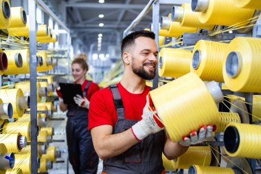 Tekstil fabrikasında çalışan bir işçi örgü makinesinin iplik makarasını değiştiriyor..