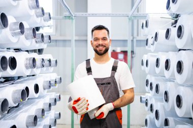 Endüstriyel örgü makinesiyle dikiş makarası tutan tekstil fabrikası işçisinin portresi.