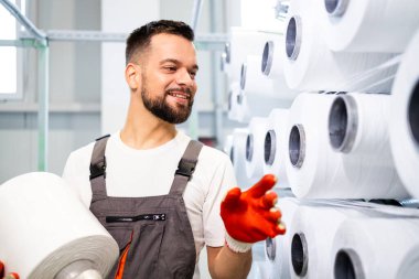 Endüstriyel örgü makinesinin makarasını değiştiren tekstil fabrikası işçisi.