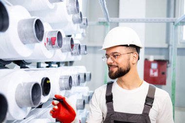 Endüstriyel örgü makinesini kontrol eden tekstil fabrikası işçisi.