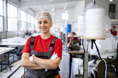 Tekstil fabrikasında dikiş makinesinin yanında duran profesyonel kadın terzinin portresi..