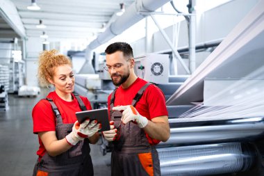 Üretim hattı çalışanları otomatik makinenin yanında duruyor ve tartışıyorlar.
