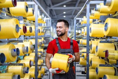 Tekstil fabrikasındaki endüstriyel örgü makinesinin iplik makarasını değiştiren bir işçi..