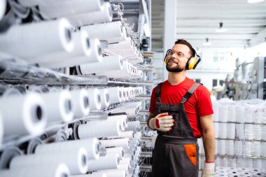 Modern endüstriyel dikiş makinesinin yanında duran tekstil fabrikası işçisi ve iplik bağlantılarını kontrol ediyor.
