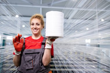 Güzel kadın fabrika işçisi tekstil fabrikasında duruyor ve elinde iplik makarası var..
