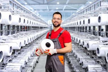 Tekstil fabrikasındaki deneyimli işçilerin portresi iplik makarası tutuyor ve endüstriyel örgü makinesinin yanında duruyor..