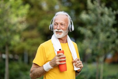 Parkta koştuktan sonra elinde havlu ve su tutan yaşlı adamın portresi..