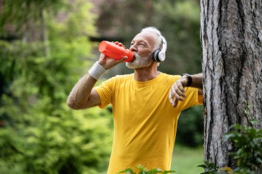 Koşu antrenmanı sırasında gri saçlı yaşlı adam su içiyor..