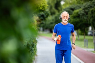 Kulaklık ve su şişesiyle sağlığına kavuşmak için koşan son sınıf öğrencisi. Emekli insanlar için eğitim.