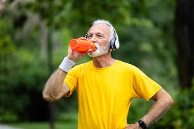 Koşu antrenmanında gri saçlı yaşlı adam su içiyor..