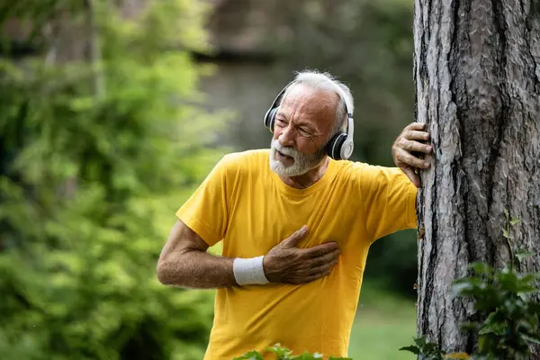 stock image Senior man having health issues and heart pain while jogging in the park.