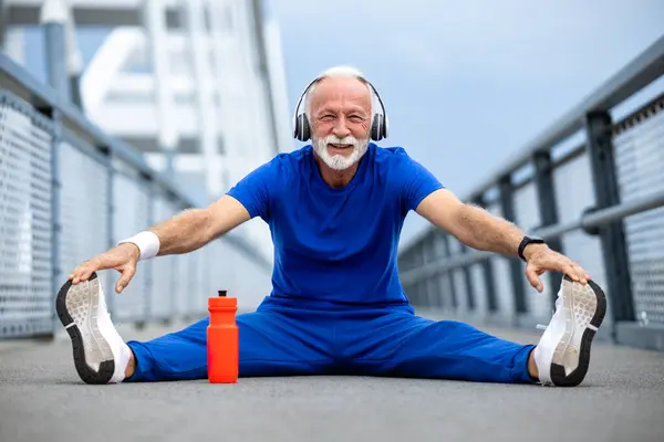 Kıdemli sporcu koşmadan önce bacaklarını açıyor ve vücudunu ısıtıyor..