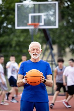 Oyuncular arka planda basketbol oynarken kıdemli koç topu tutuyor..