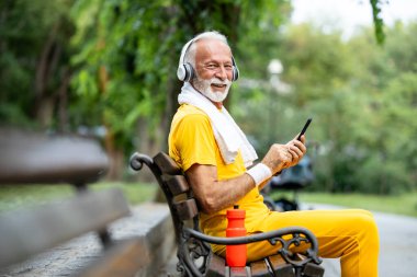 Eğitimden sonra bankta oturan ve akıllı telefon kullanan kıdemli bir adam..