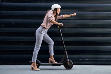 Elektrikli scooter kullanan güzel bir kadın. Kolunu dümdüz tutuyor..