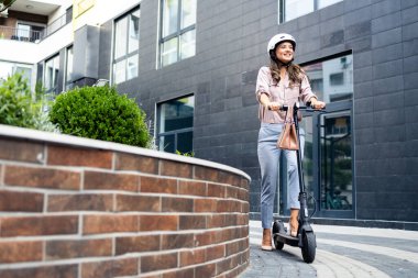 Gülümseyen kadın şehirde elektrikli scooter sürmekten hoşlanıyor..