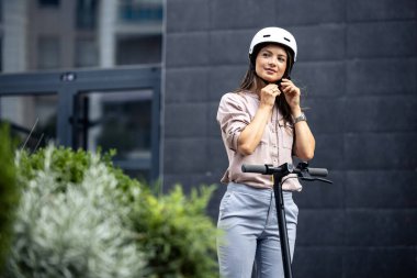 İşe giderken elektrikli scooter sürmeden önce kask takan güzel bir kadın..