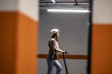 Kasklı, kendinden emin bir kadın yeraltı garajında elektrikli scooter kullanıyor..