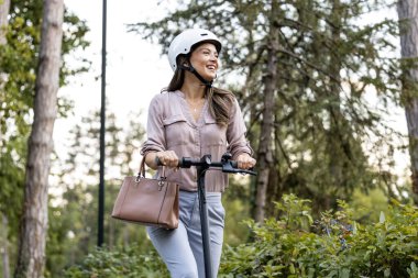 Parkta elektrikli scooter kullanan kasklı güzel bir kadın..