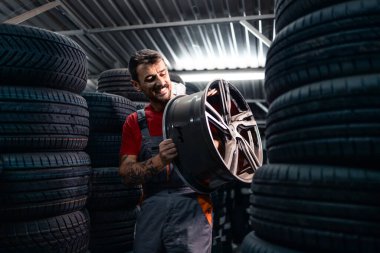 Depoda tekerlek kenarı taşıyan ve lastik envanterini düzenleyen bir işçi. Ulaşım endüstrisi ve araba parçaları.