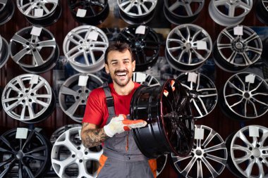 Araba tamircisi lastik atölyesinin içinde yepyeni tekerlek kenarı tutuyor..