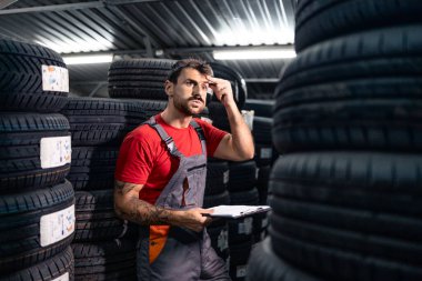 Çalışkan bir çalışan depodaki araba lastiklerinin envanterini düşünüyor ve kontrol ediyor..