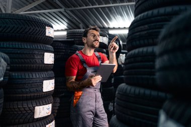 Depoda çalışan biri lastik servisi atölyesinde araba lastiği arıyor..