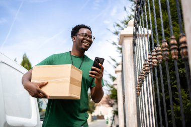 Mutlu postacı akıllı telefonunun adresini kontrol ediyor ve paketleri teslim ediyor..