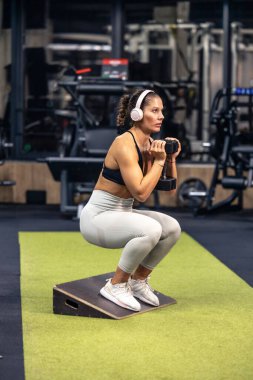 Spor salonunda ağırlık kaldırarak çömelme antrenmanı yapan sağlıklı bir kadın..