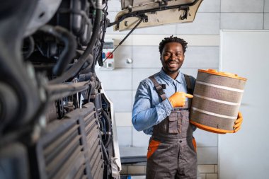 Profesyonel kamyon tamircisi aracın yanında duruyor ve motor hava filtresi tutuyor..