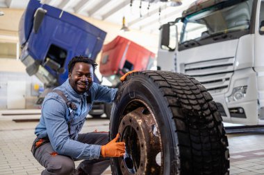 Gülümseyen tamirci garajın içinde bozuk kamyon tekerleğini değiştiriyor..