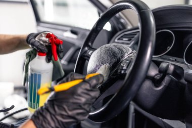Profesyonel temizlikçi, arabanın direksiyonunu ve içini temizlemek için fırça kullanıyor. Araç ayrıntıları.